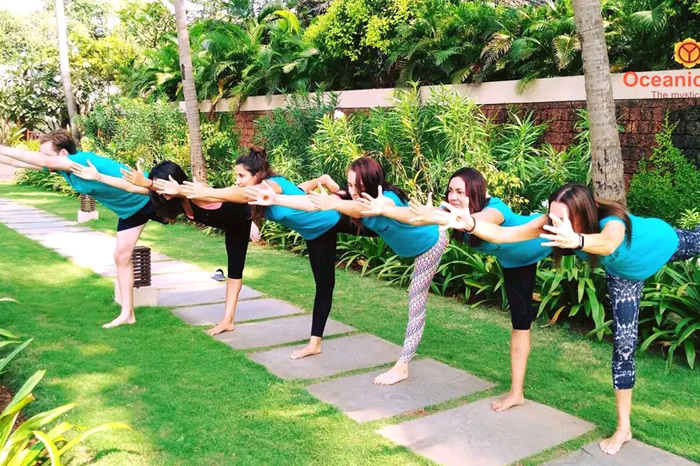 "Yoga practitioners during a 100-hour yoga teacher training in Thailand, performing asanas in a tranquil outdoor setting with vibrant greenery and a peaceful atmosphere, promoting spiritual growth and holistic wellness."